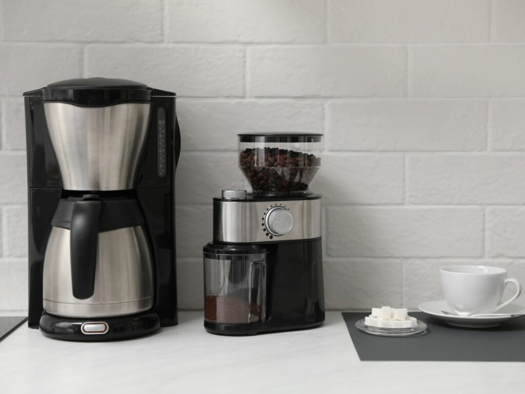 A coffee grinder and a thermal coffee maker on a counter.