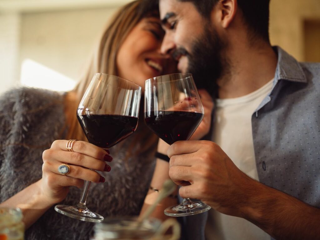 A man and woman with red wine glasses in a restaurant.