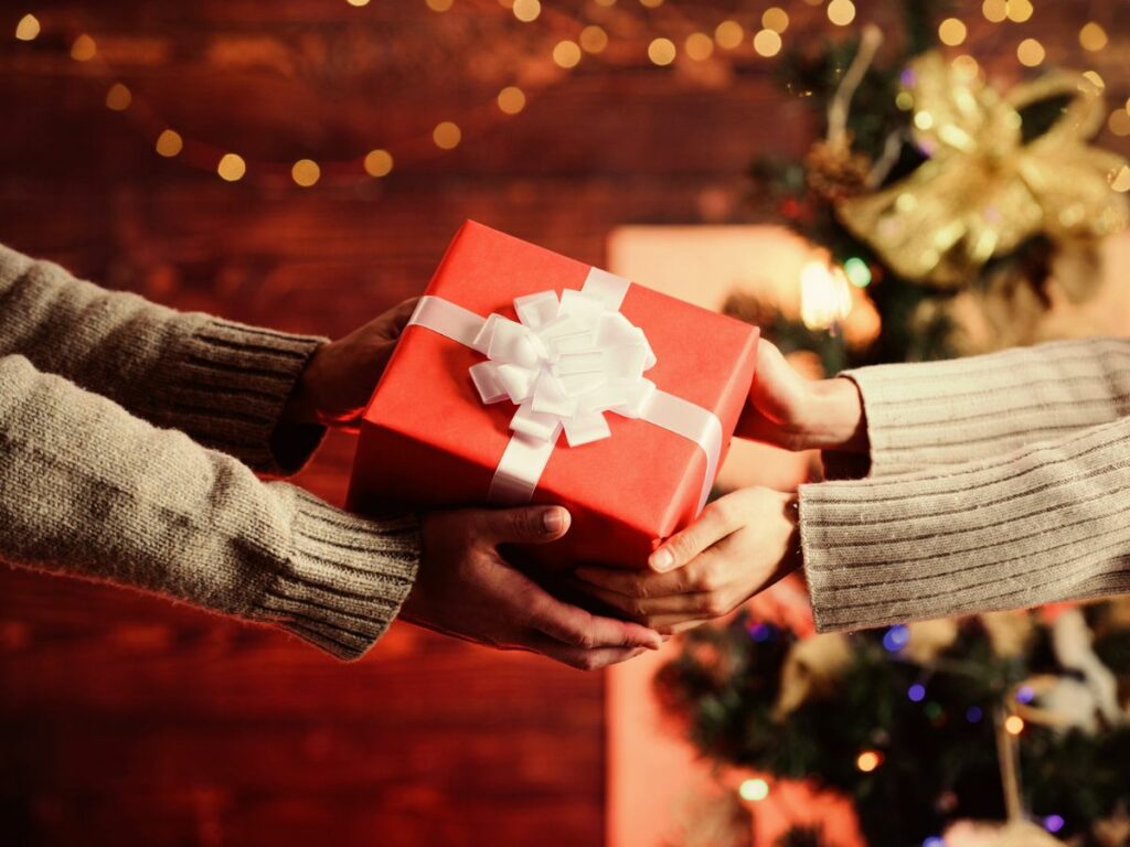 Two people exchanging a red gift box in front of a christmas tree.