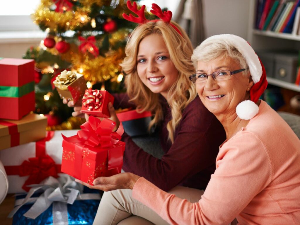 A mother and daughter holding christmas presents in front of a christmas tree.