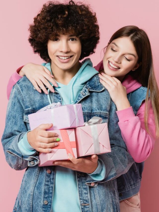 Young couple holding gift boxes on pink background.