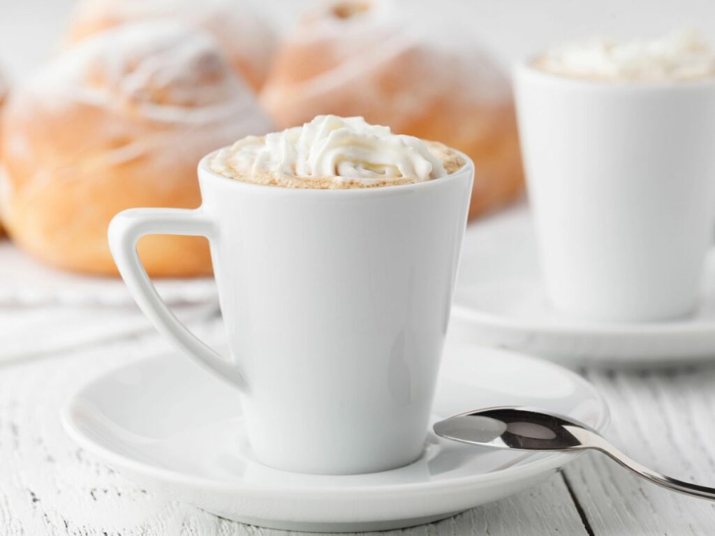 Two cups of eggnog coffee with whipped cream and cinnamon rolls.