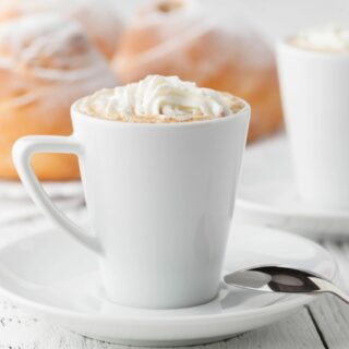 Two cups of eggnog coffee with whipped cream and cinnamon rolls.
