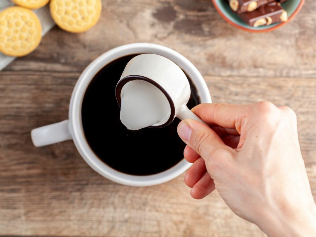 A person pouring creamer into coffee.