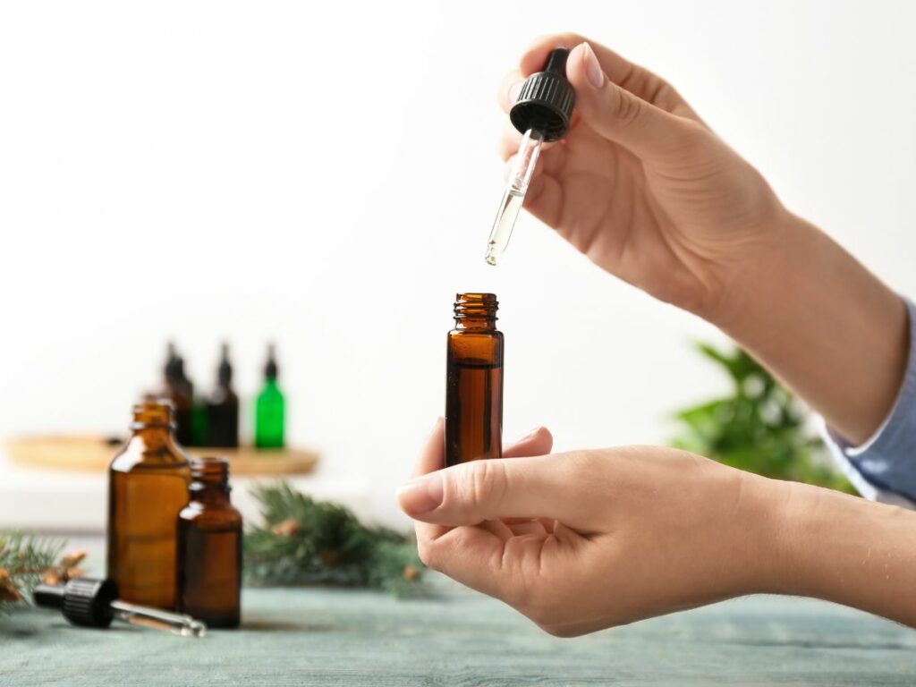 A person pouring essential oil into a glass bottle.