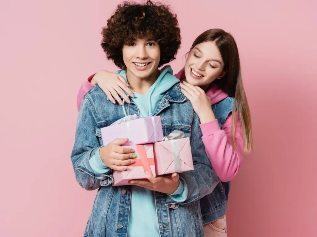 Two young teens hugging each other with gifts in hand.