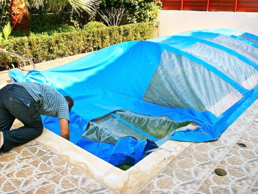 A man putting a blue cover over a pool.