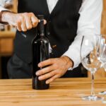 A bartender opening a wine bottle next to wine glasses.