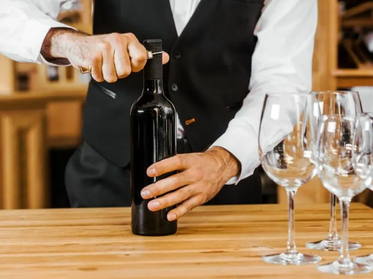 A bartender opening a wine bottle next to wine glasses.