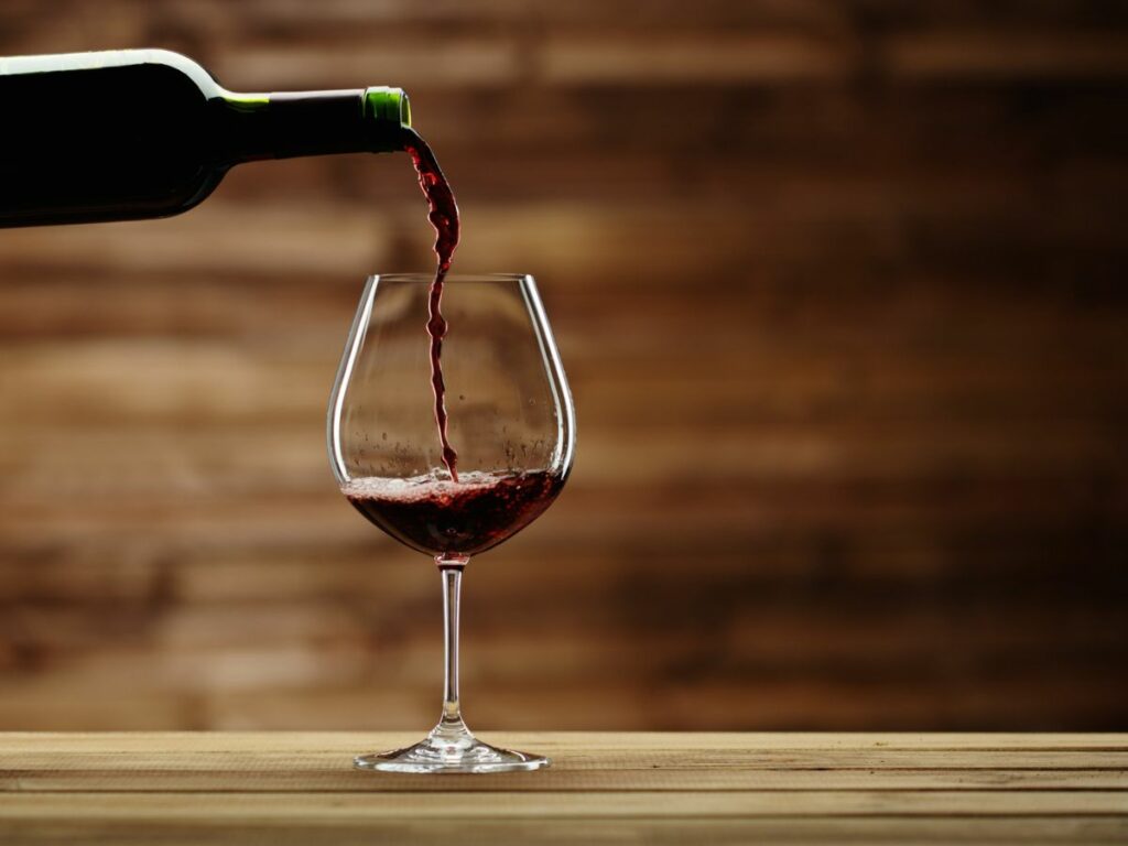 A bottle of red wine is being poured into a glass.