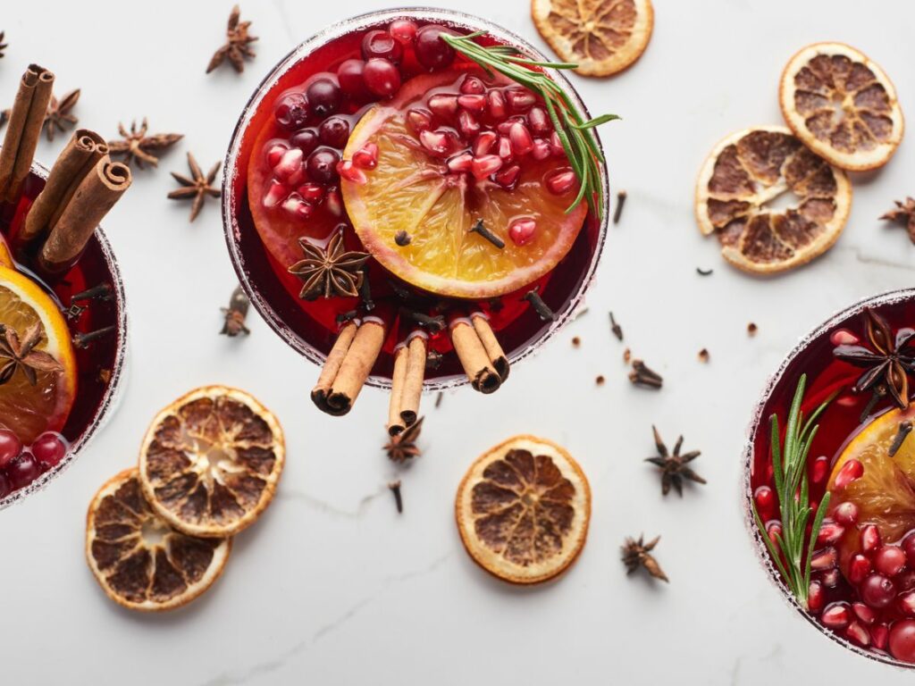 Three glasses of mulled wine with oranges, cinnamon, and star anise.