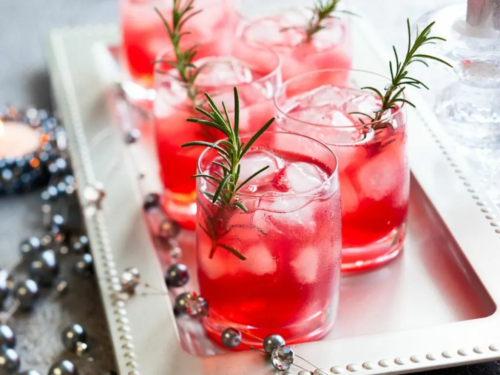 A tray of drinks with rosemary sprigs in them.