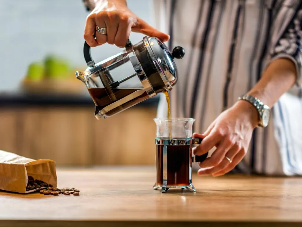 A woman pouring coffee into a french press.
