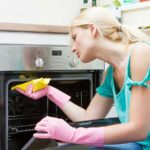 A woman in pink gloves cleaning an oven.