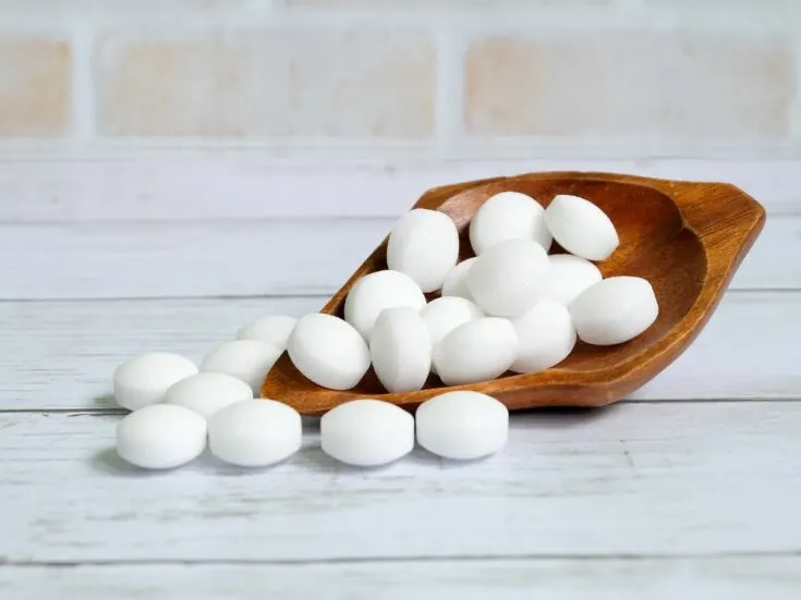 White mothballs in a wooden bowl on a white background.