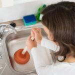 A woman unclogging a kitchen sink.