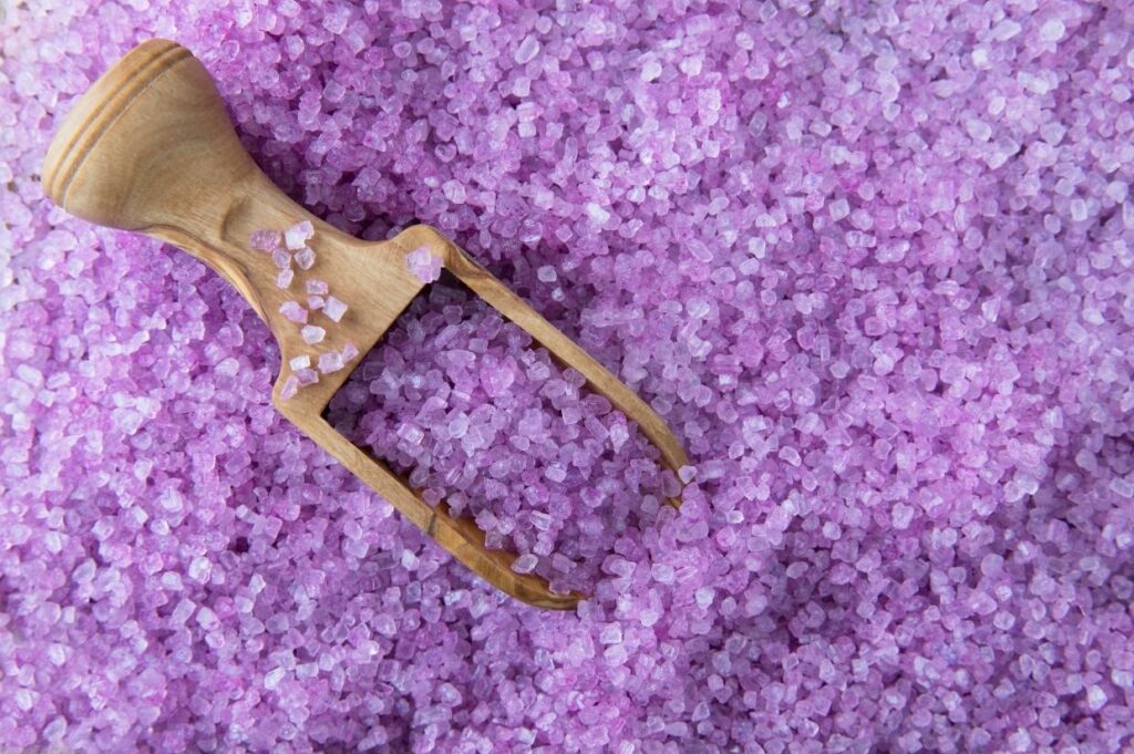 A wooden spatula is laying on top of purple lavender salt.