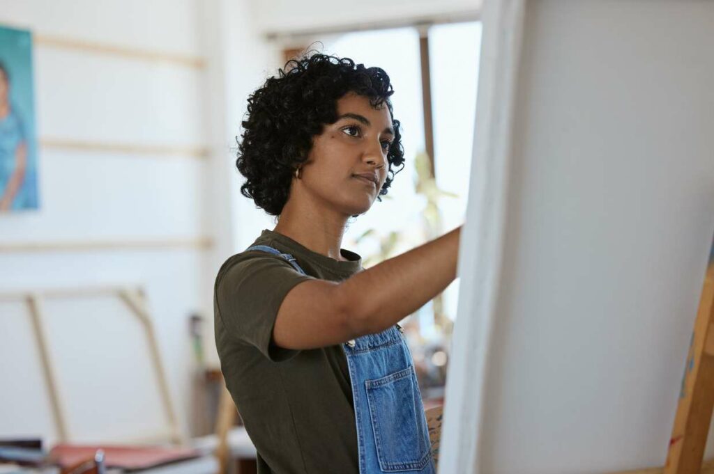 A woman in overalls is painting on an easel.