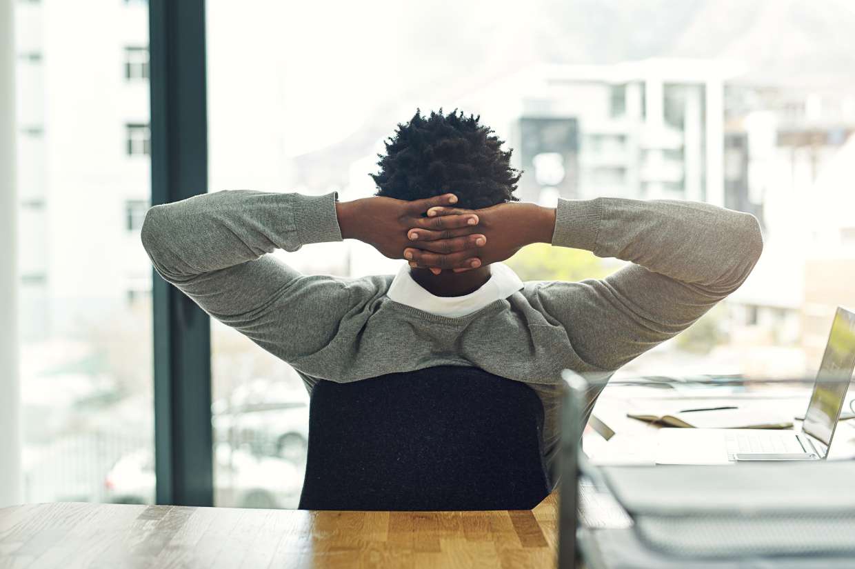 A man relaxes at his desk in front of a window.