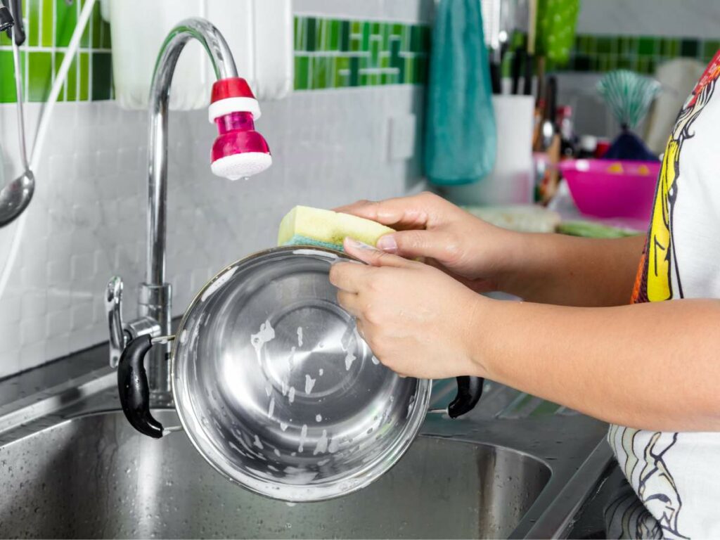 A woman is washing a pan in a kitchen sink.