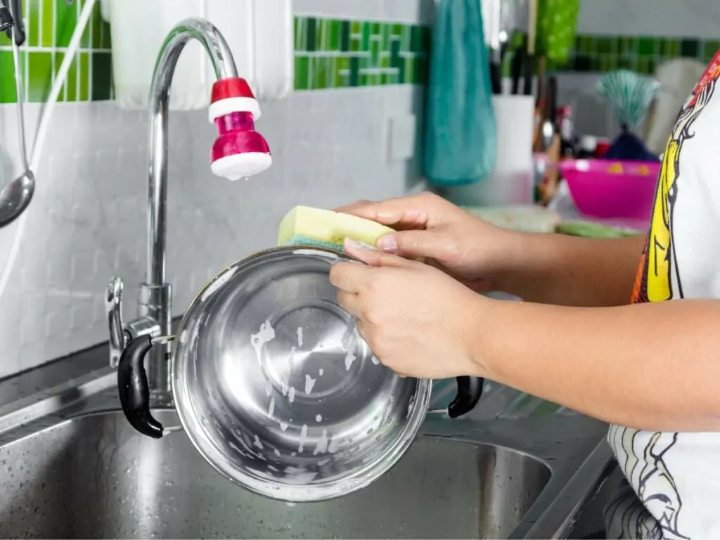 A woman is washing a pan in a kitchen sink.