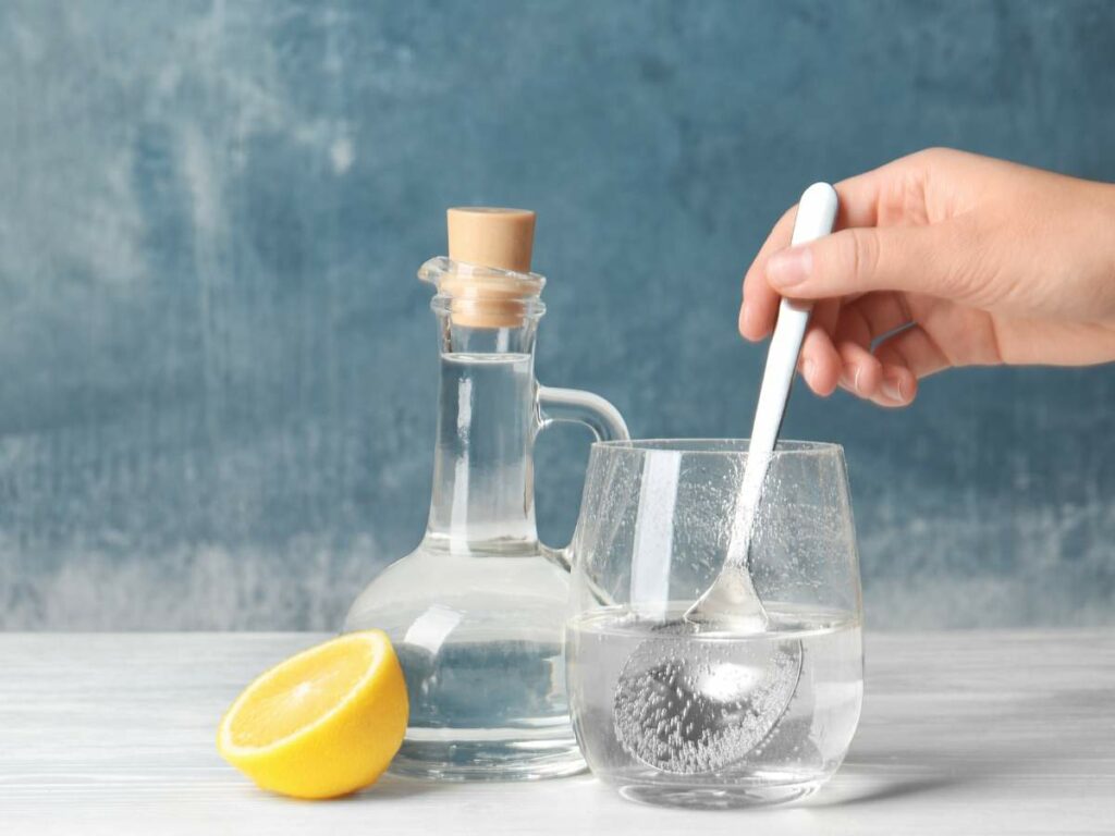 A hand mixing a glass of water and a lemon.