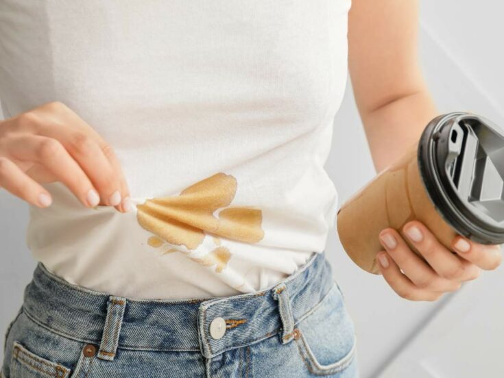 A woman holding a coffee cup with a stain on her shirt.