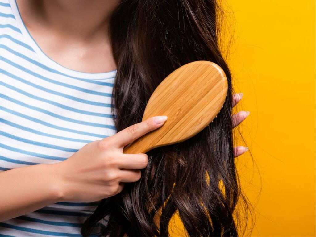 A woman is combing her hair with a wooden brush.