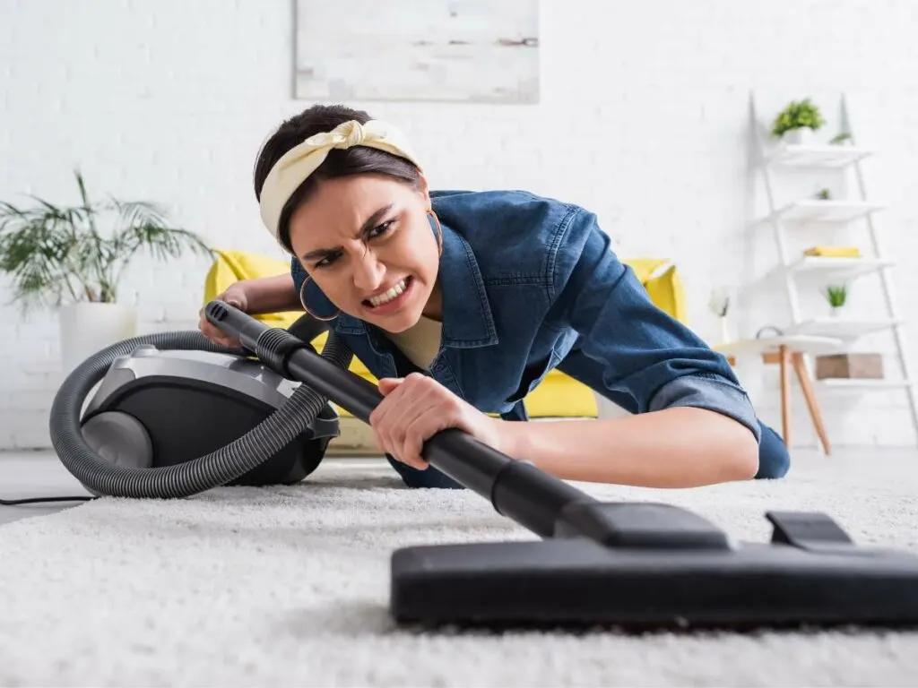 Woman looking frustrated while vacuuming the carpet.