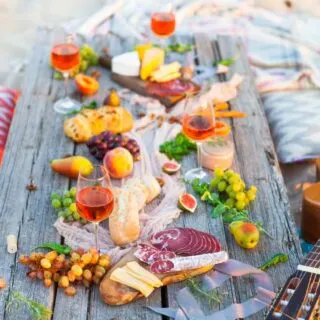 Beach picnic with a variety of snacks and wine on a charcuterie board, accompanied by a guitar.
