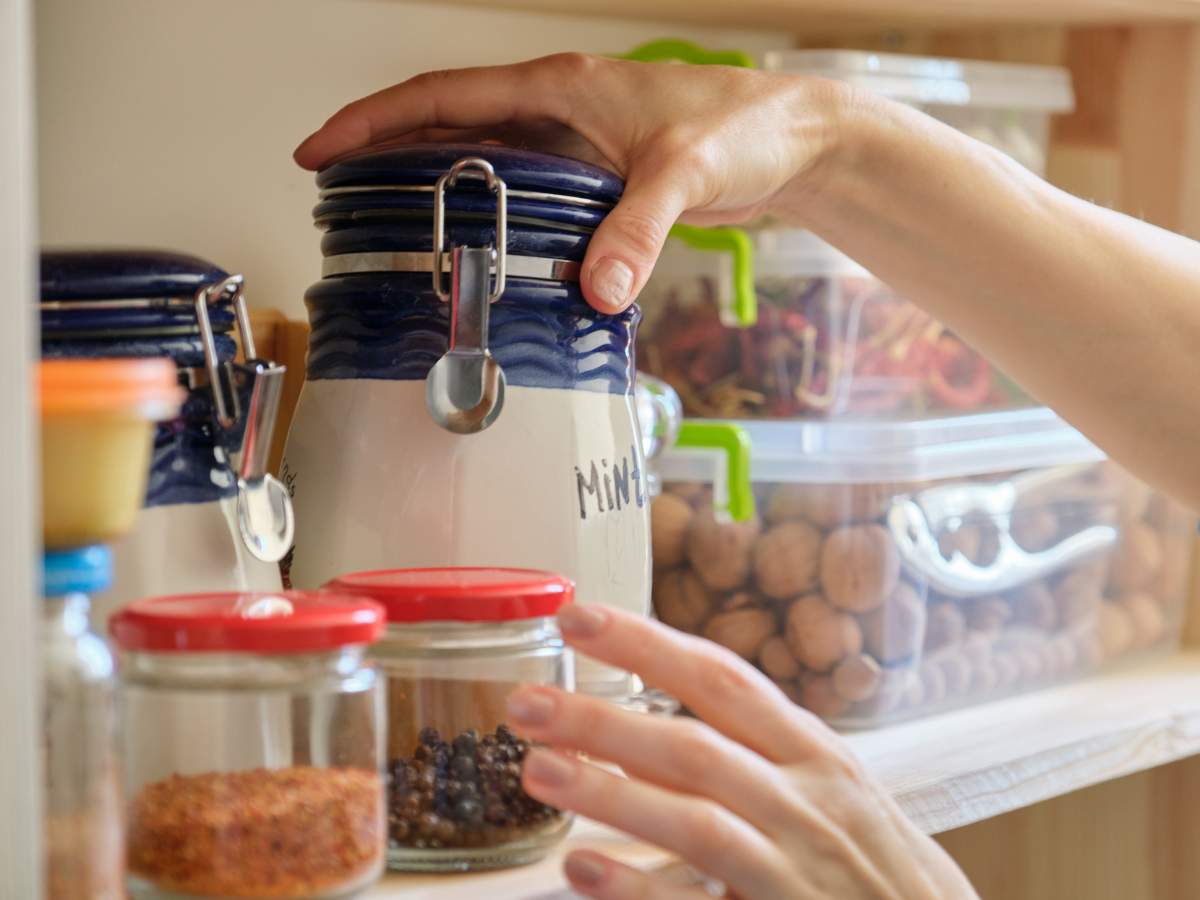 A woman is putting spices into a jar on a shelf.