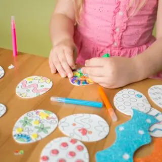Child coloring easter egg cutouts on a table.