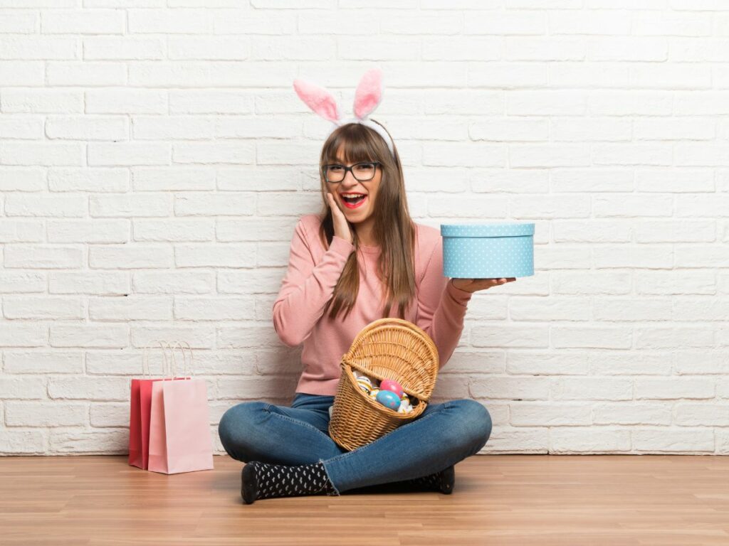 Teen in bunny ears sitting with a basket of easter eggs and a gift box.