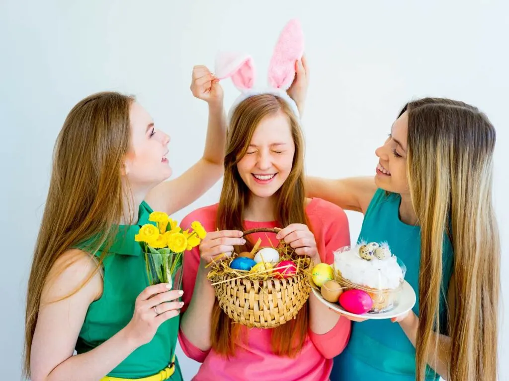 Three women celebrating easter with bunny ears, colorful eggs, and spring flowers.