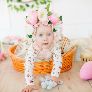 A baby with a floral headband crawls near a wicker basket and easter eggs.