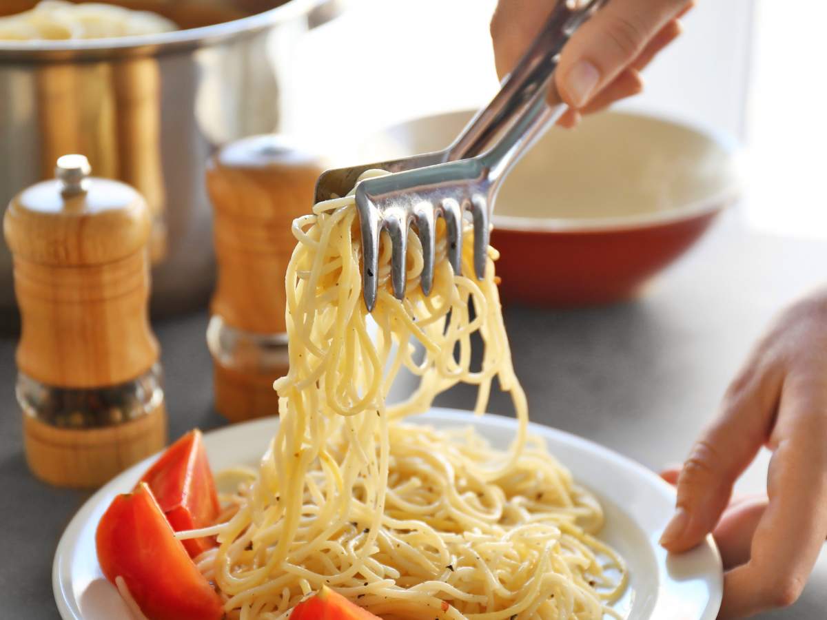 Hands using a pasta fork with a bowl of noodles.