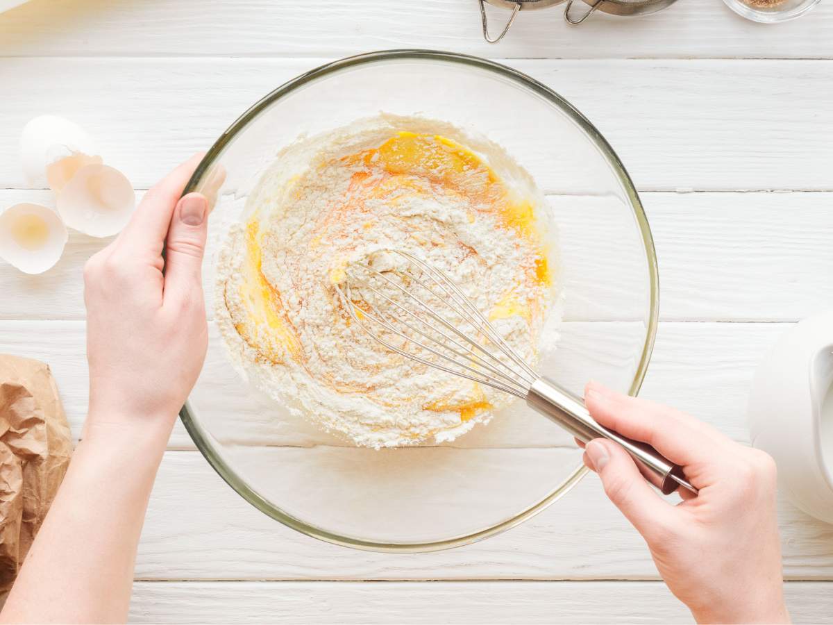 Person whisking flour in a glass bowl.