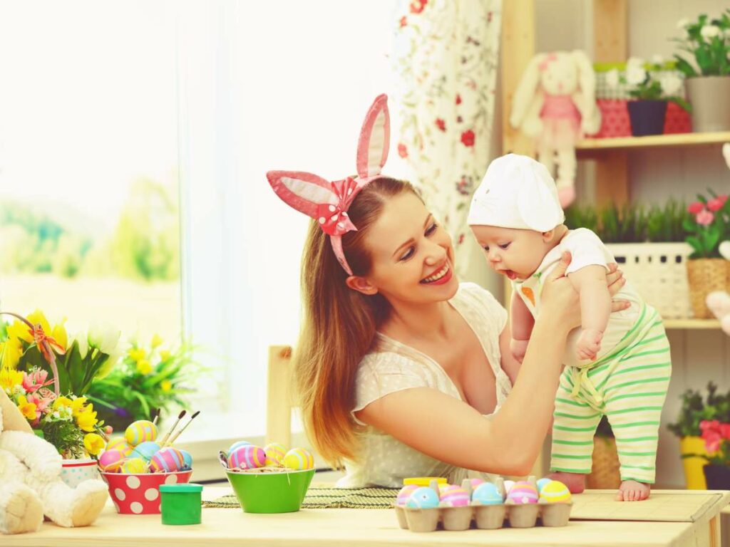 A woman holding a baby in front of a table decorated for Easter.