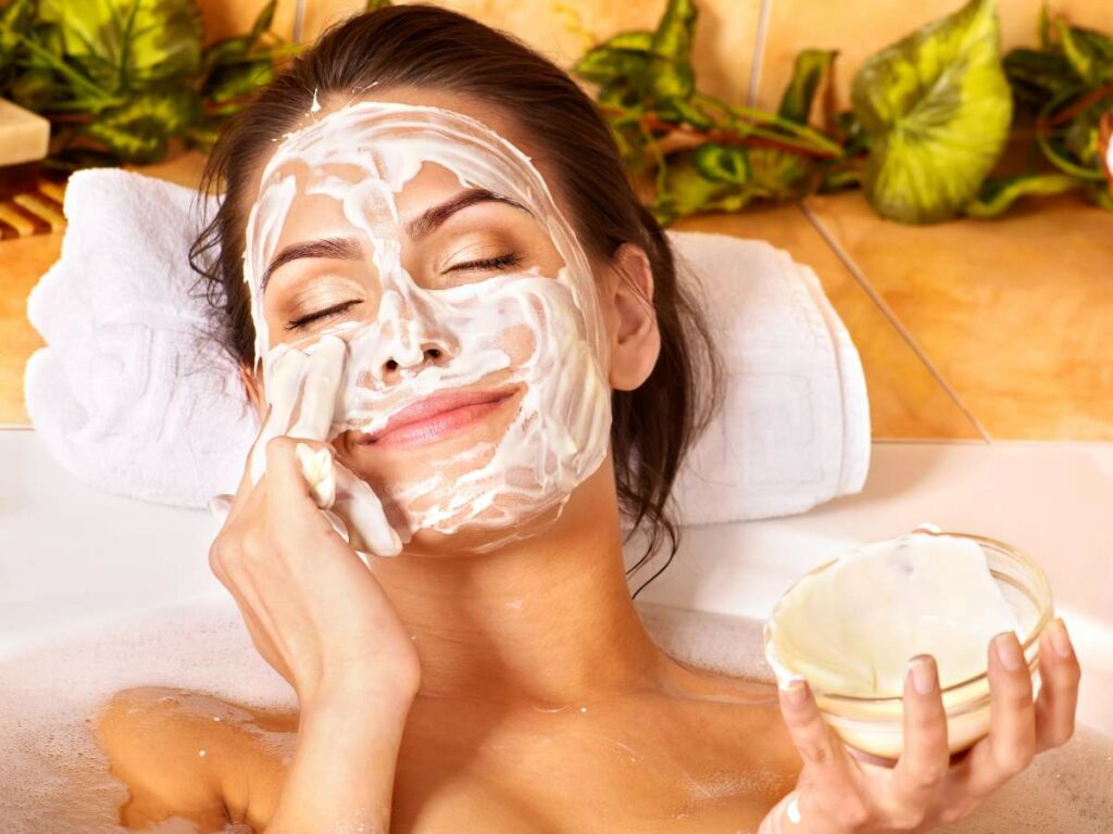 A woman using a facial mask in a bath tub.