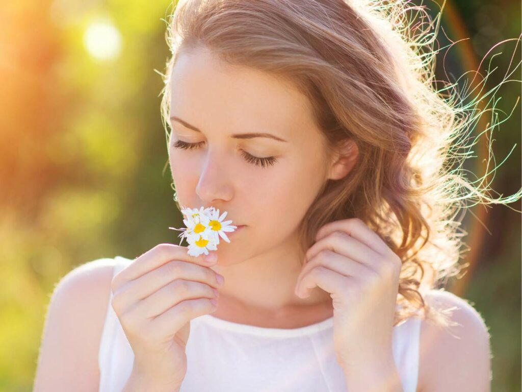 A woman smelling a daisy in the sun.