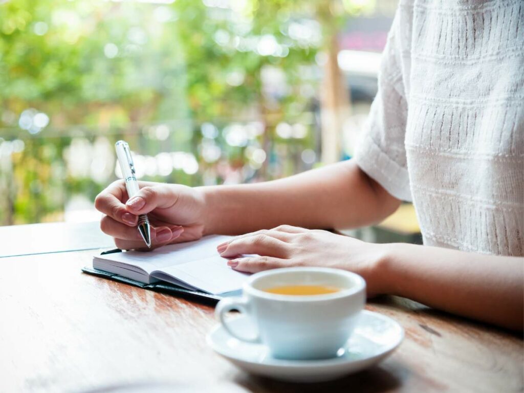 A woman writing in her journal with a cup of tea.