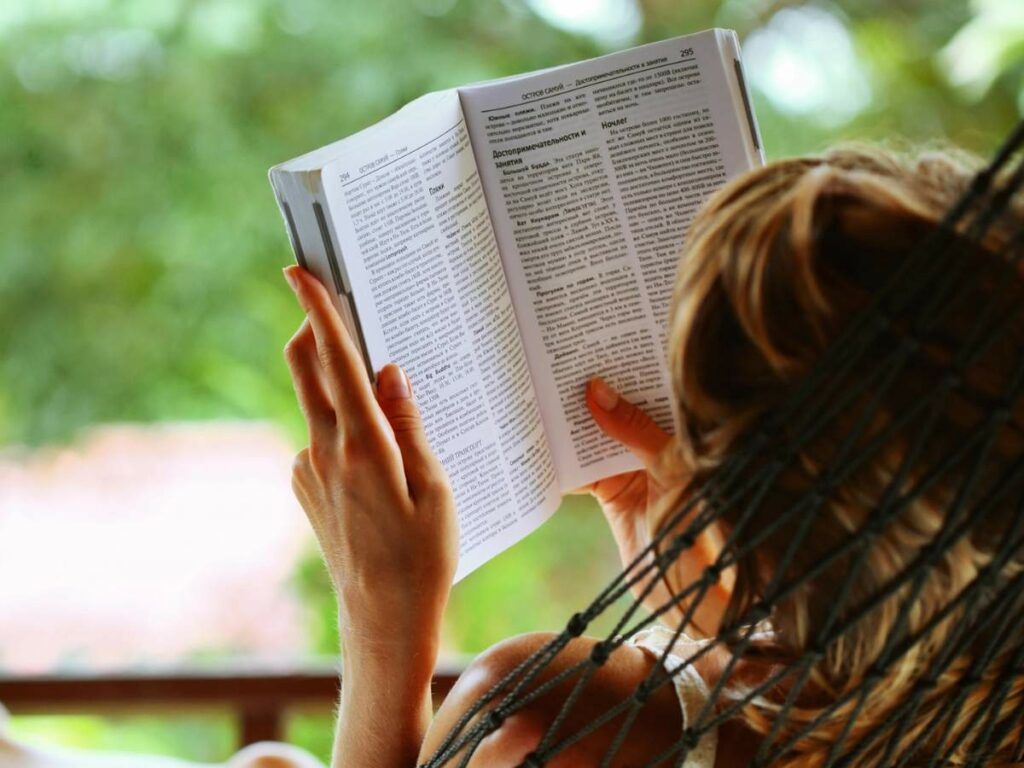 A woman reading a book in a hammock.