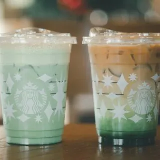 Two green starbucks drinks on a wooden table.