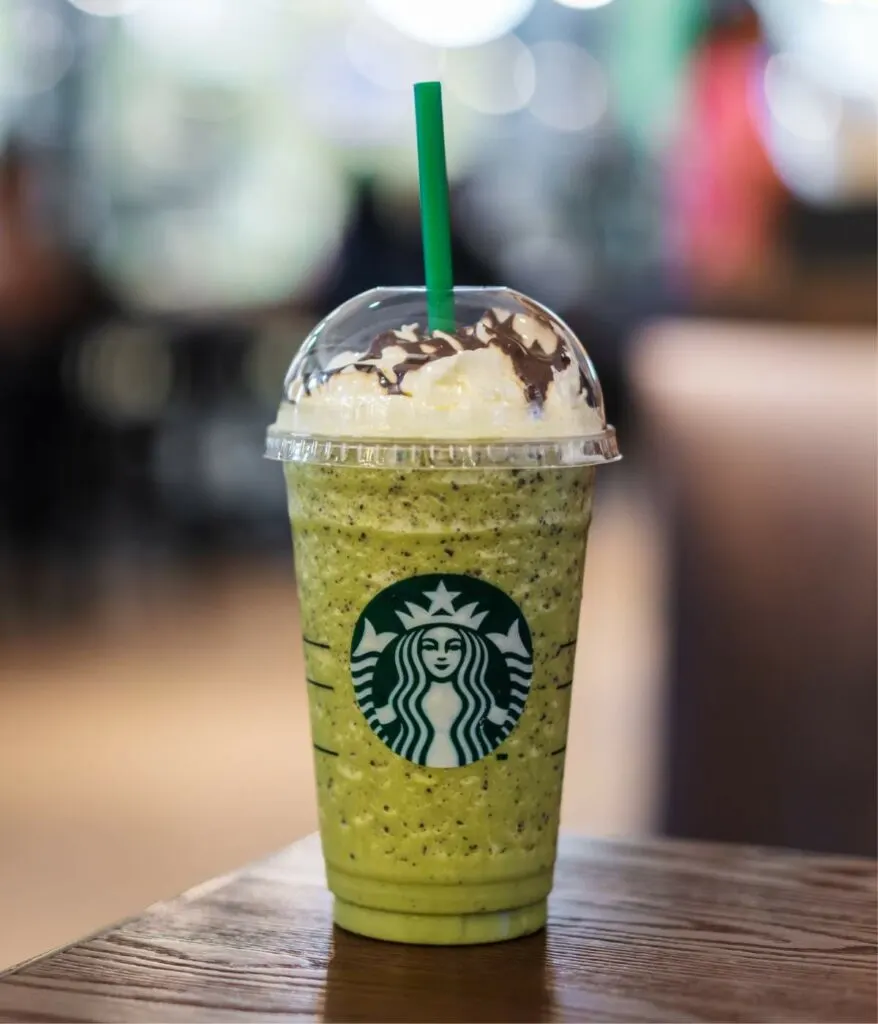 A green starbucks drink with a straw on a wooden table.