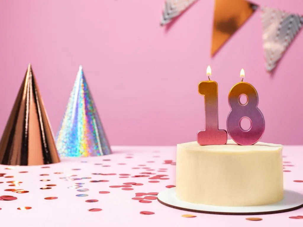 A birthday cake with "18" candles, party hats, and confetti on a pink background.