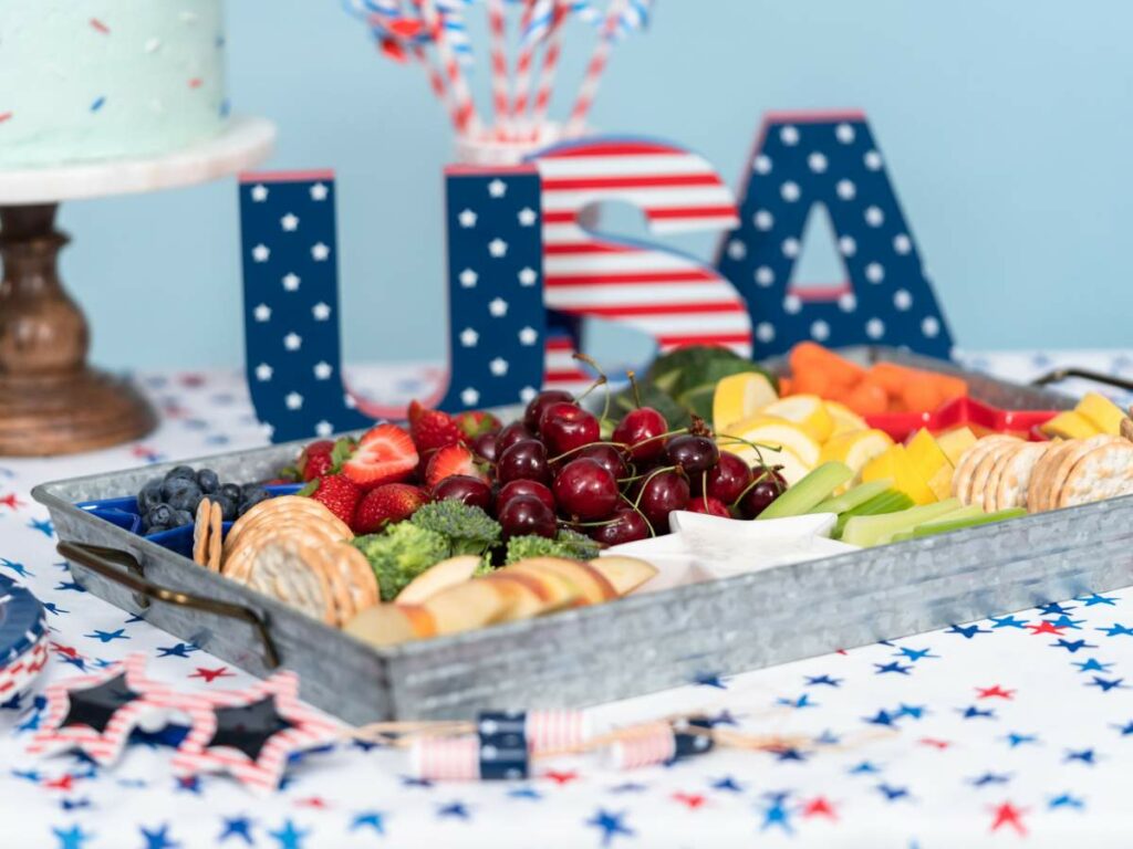 A vibrant display of fruit arranged in a tray at a patriotic-themed event with decorative "usa" letters in the background.