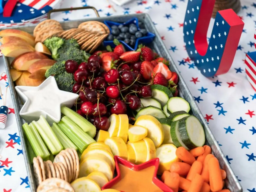 A colorful assortment of fresh fruits and vegetables arranged neatly on a charcuterie board with a patriotic-themed table setting.