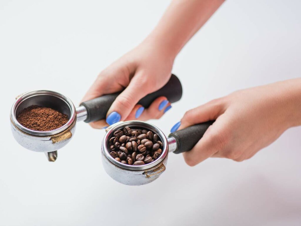 Two hands holding espresso portafilters filled with ground coffee and whole coffee beans.