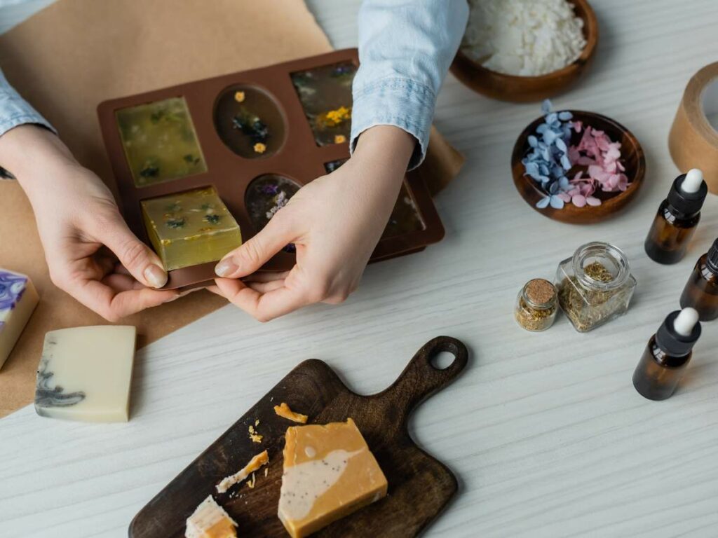 Person making handmade soap with natural ingredients and essential oils on a wooden table.