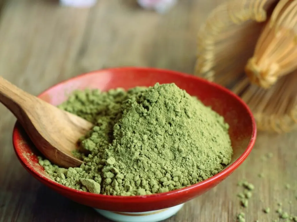 A bowl of green matcha powder with a wooden spoon.
